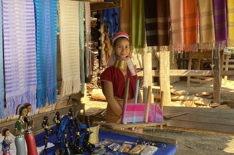 Mujer jirafa de la etnia kayan vendiendo artesanía tradicional en el norte de Tailandia