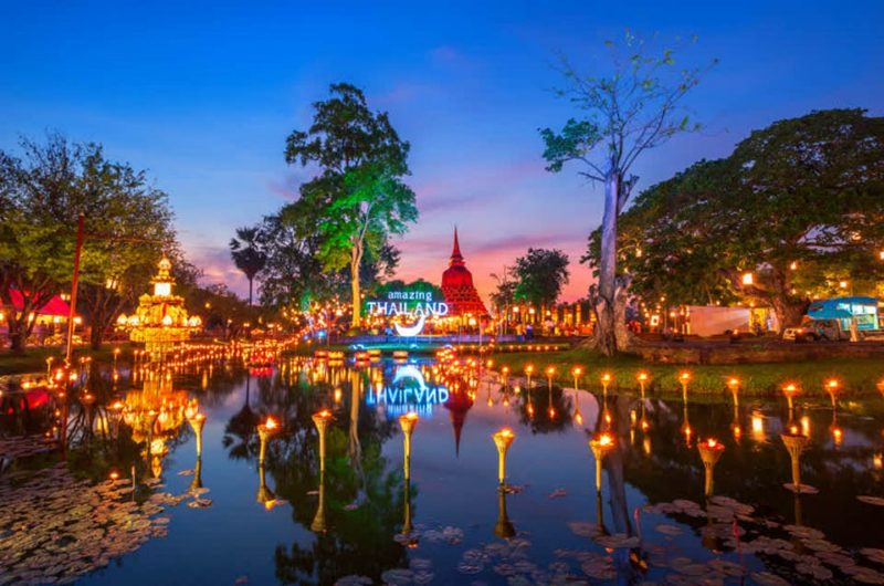 Velas flotando frente a un templo iluminado en Sukhothai durante Loy Krathong