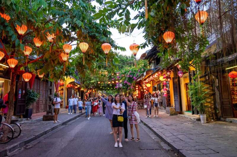 Turistas paseando por una calle iluminada con faroles en el centro histórico de Hoi An