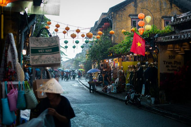 Calle del casco antiguo de Hoi An en octubre con varios visitantes caminando bajo paraguas
