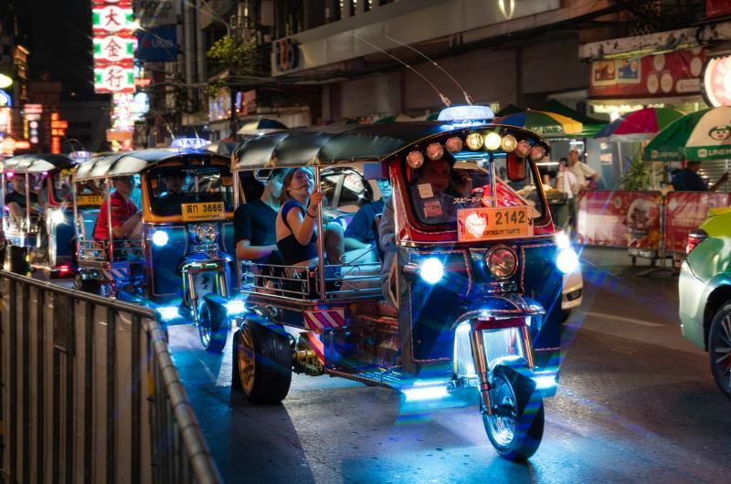 Turistas en un tuk tuk por la noche en Chinatown de Bangkok