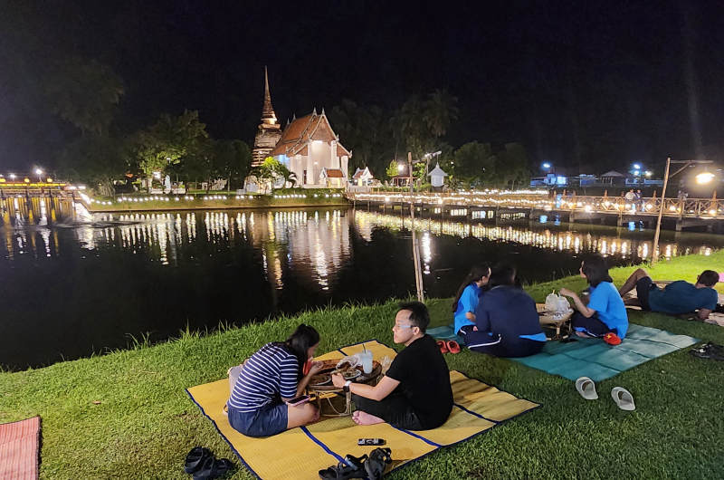 Personas comiendo en el suelo sobre esterillas junto al mercado nocturno de Sukhothai