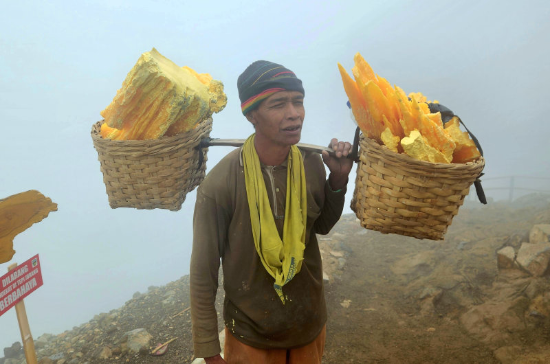 Minero de azufre cargando bloques de azufre en el cráter del Monte Ijen en Java