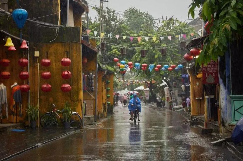 Persona con impermeable en bicicleta durante una intensa lluvia del monzón en Hoi An, Vietnam